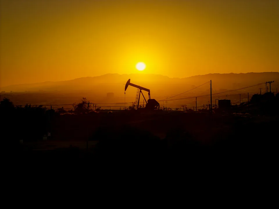 A distant pump jack against an amber sky and low hills