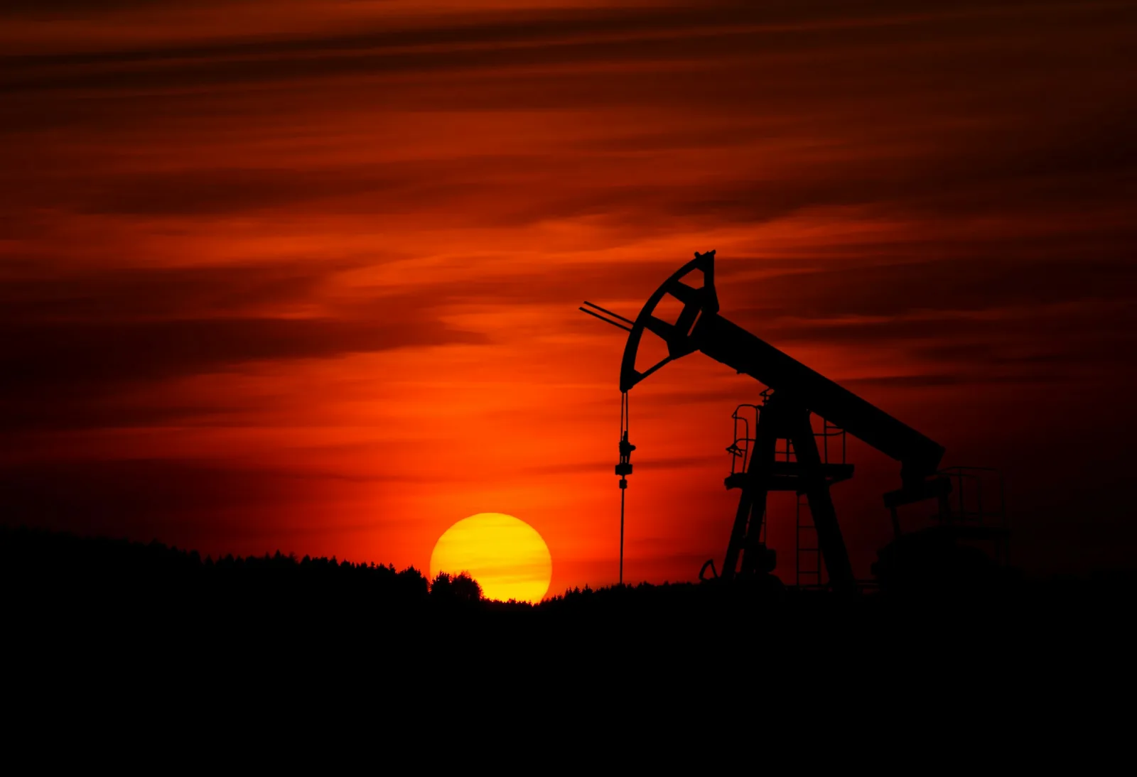 A pump jack silhouetted against a deep red sunset over flat open country