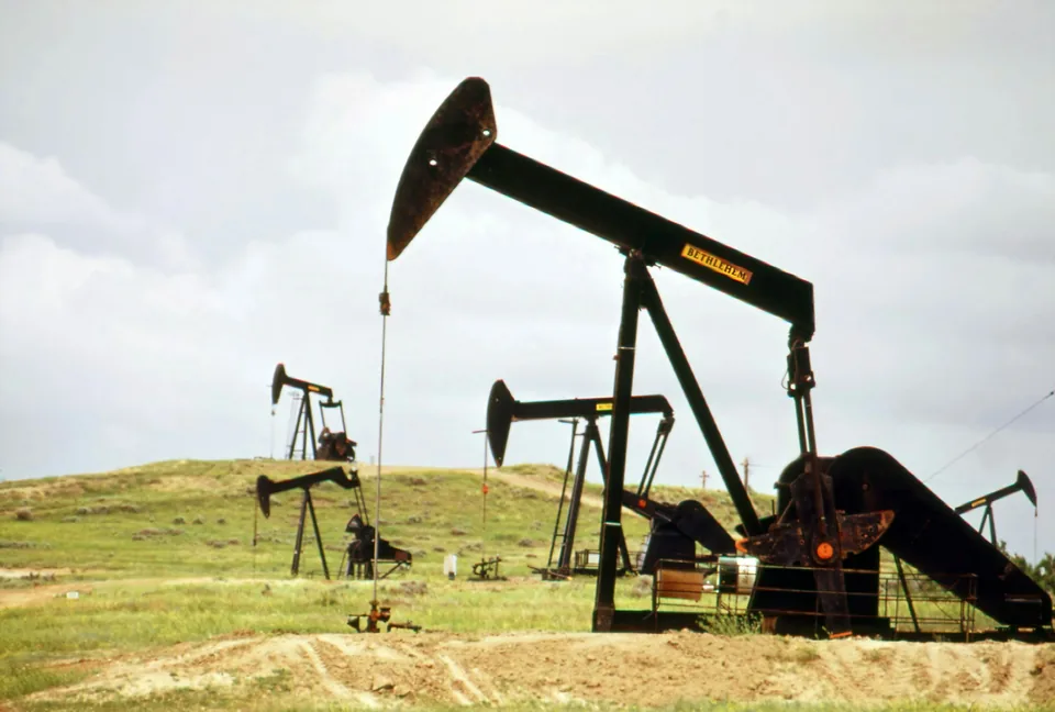 A large pump jack on a green hillside with more pump jacks behind it